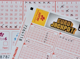 Three lottery tickets are displayed, including Eurojackpot and Super 6. Various numbers are marked on the tickets, with some crossed out and others checked. The Eurojackpot ticket is partially visible with the logo prominently displayed, and a ticket number is visible on one of the tickets.