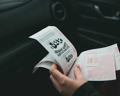 A person is holding and examining what appears to be lottery tickets inside a car. The image is focused on the tickets and the person's hands, with parts of the car interior visible in the background.