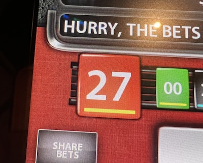 A digital display screen showing a casino betting interface, with text prompting to hurry bets and a highlighted number 27 in red. There are options for betting amounts and a 'share bets' button.